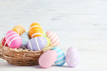 Colorful easter eggs in basket on white wooden background