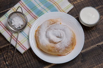 On a wooden table a vertuta sprinkled with powdered sugar and a towel, next to it is a bowl with white sauce