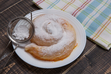 Ready-made vertuta with pumpkin lies on a plate, sprinkled with powdered sugar, a towel is nearby