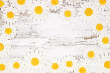 Frame of white daisy flower paper decorations. Above view over a rustic white wood background. Copy space.