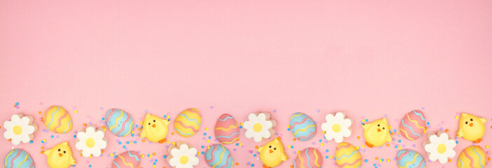 Easter candy bottom border. Colorful pastel candy eggs, chicks and flowers. Top down view against a pink banner background. Copy space.