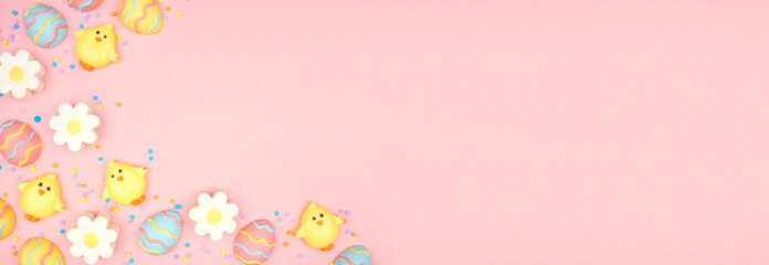 Easter candy corner border. Colorful pastel candy eggs, chicks and flowers. Above view against a pink banner background. Copy space.