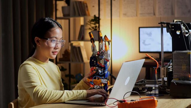 Teen Asian Girl Checking And Comparing A Cyborg Hand To The Picture On A Laptop At Home While At Home
