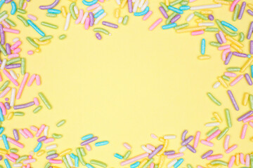 Fototapeta na wymiar Colorful candy sprinkles frame. Overhead view on a yellow background. Pastel Easter color theme. Copy space.