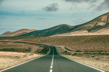Charming cinematic road in Spain with vehicle in the distance with desert on both sides and beautiful cloudy blue sky perfect summer travel hot weather