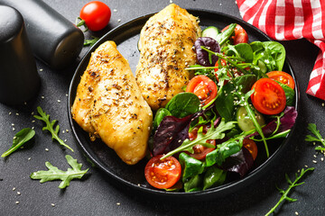 Fresh salad with chicken fillet and vegetables on black plate.