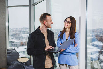 Two business people working remotely online using a laptop. Colleagues work in the workspace remotely standing near the window.