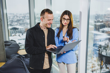 Two business people working remotely online using a laptop. Colleagues work in the workspace remotely standing near the window.