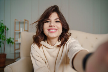 Pretty young asian female with big smile sitting at living room. She having fun taking selfie.