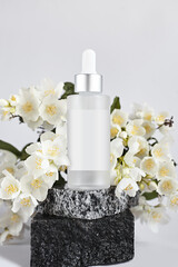 Glass bottle with a pipette on a background of white flowers. Mockup packaging with a label for cosmetics on a white background.