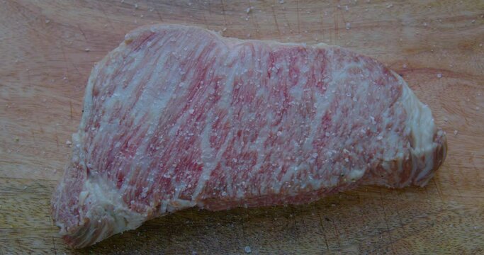 Wagyu Steak A5 is salted and peppered on a wooden cutting board a closeup shot

