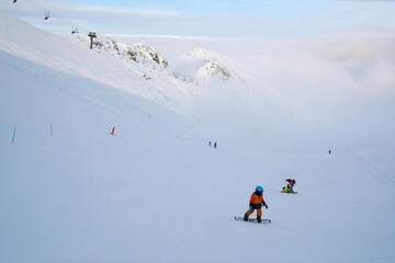 Little child on snowboard on Kasprowy Wierch Peak in Tatras Mountains, famous place in Tatras with cable railway. Poland. Tatra National Park