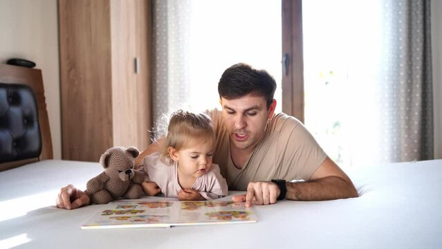 Dad reading a book to a little girl pointing a finger at pictures