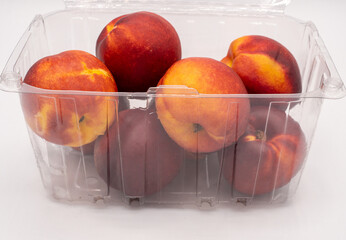 Nectarines in a plastic container on a white background.