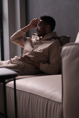 Fototapeta premium Portrait of a cheerful young african american man 20s wearing casual hoody and glasses sitting on sofa against black background. copy space isolated