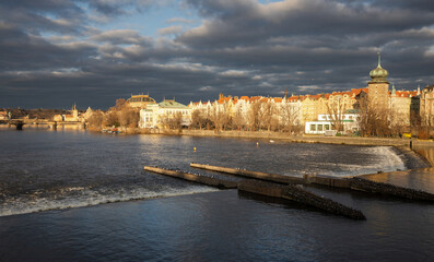 Obraz premium Winter evening with dark clouds and the setting sun by the river in the center of Prague