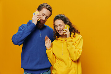 Woman and man cheerful couple with phones in hand talking on cell phone crooked smile cheerful, on yellow background. The concept of real family relationships, talking on the phone, work online.
