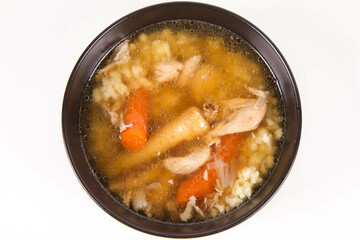 Chicken soup with noodle and carrot and parsley roots, chicken meat visible, in a bowl on a white background