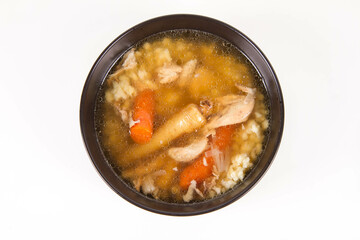 Chicken soup with noodle and carrot and parsley roots, chicken meat visible, in a bowl on a white background