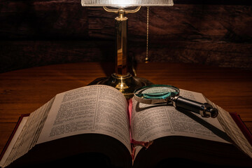 open bible on oak table with magnifying glass and desk lamp