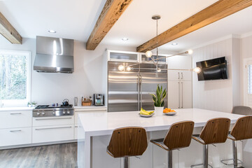 A large luxury modern kitchen with white walls and wood beams and a large quartz quartzite island