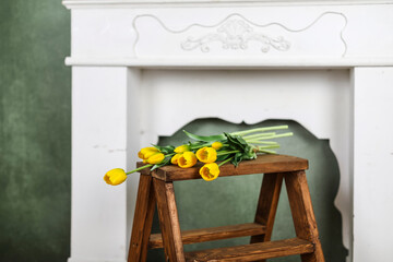 Yellow tulips flowers spring bouquet on a wooden ladder in vintage interior with white ornamental fireplace portal