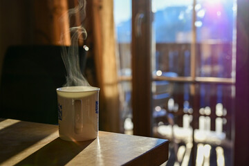 steaming mug of tea in front of a window with sunlight shining into the room