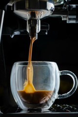 Beautiful caramel-colored espresso being extracted in a clear glass cup.
