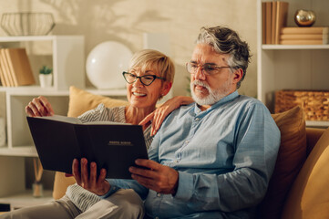 Senior couple looking at photo album and sitting on a couch at home