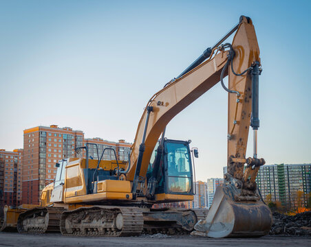 The tracked orange backhoe loader is parked with the bucket lowered. The crawler excavator is parked on the street.