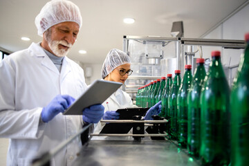Experienced quality control workers controlling production of bottled drinking water in beverage...