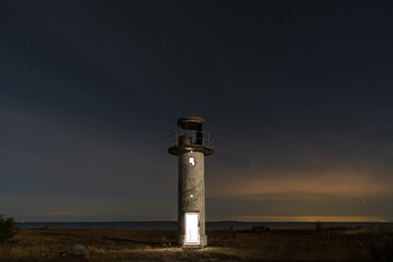 Night scene.  An old luminous lighthouse on the shore of the Baltic Sea under the starry sky.