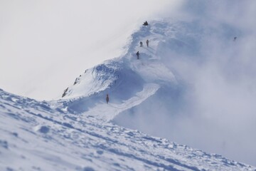 Little silhouettes of skiers on slope in cloudy scenery, Kasprowy Wierch Peak in Tatras Mountains. Tatra National Park, Poland