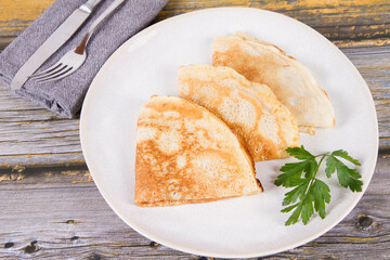 Portion of crepes decorated with a parsley leaf on a wooden table