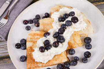 Crepes with blueberry fruit and whipped cream on a wooden background