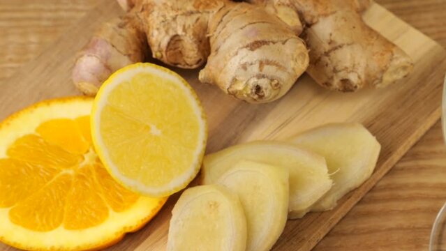 Cooking a drink of citrus and ginger to boost immunity. Lemonade is poured into a glass against the background of slices of orange, lemon and ginger. Slow motion.