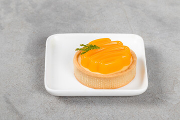 Round tangerine tartlet with custard cream and curly tangerine jelly. On a plate. Light grey background