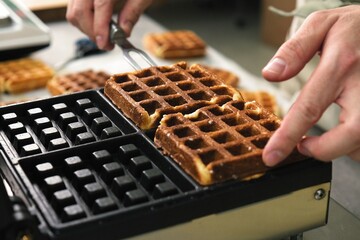 belgian waffles in a waffle iron. the cook pulls the finished Belgian waffles out of the oven