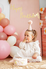 Fototapeta na wymiar Cute baby eating cake for first birthday. Baby girl in dress. Festive decor in pink colors