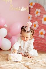 Cute baby eating cake for first birthday. Baby girl in dress. Festive decor in pink colors