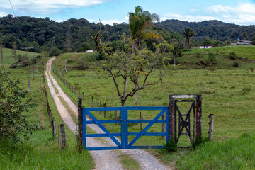 Blue farm gate with dirt road and trees in countryside of Sao Paulo state, Brazil