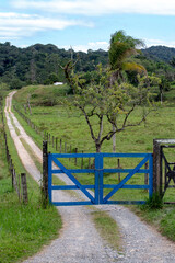 Blue farm gate with dirt road and trees in countryside of Sao Paulo state, Brazil