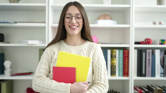 Young beautiful hispanic woman standing holding books at library university