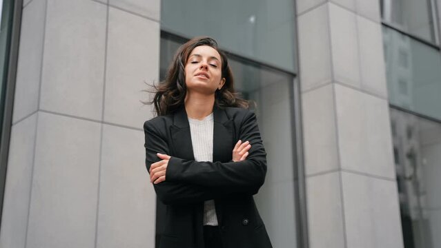 Woman Caucasian with long dark hair and black suit turning to the camera, smiling, and putting her hands on her chest. Back view, close up, slow motion.