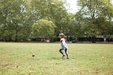 Fototapeta premium Little girl playing football in the park