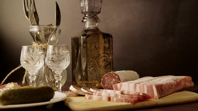 Stylized still life with a bottle of vodka or moonshine with a glass, bacon, sausage and cucumber.