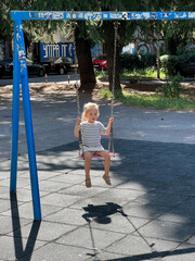 Little girl sits on a chain swing on the playground