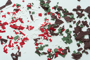 red, white, brown, and green cut paper shapes or confetti photographed from above on blank paper