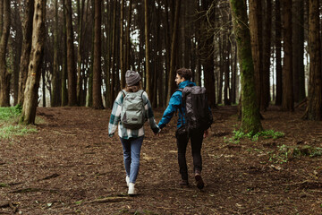 Millennial caucasian guy and woman in jackets and backpacks travel in cold forest, enjoy adventure