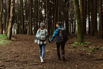 Fototapeta premium Millennial caucasian guy and woman in jackets and backpacks travel in cold forest, enjoy adventure